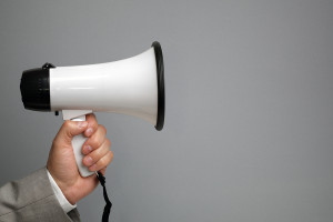 Businessman holding a megaphone in front of blank gray backgroun
